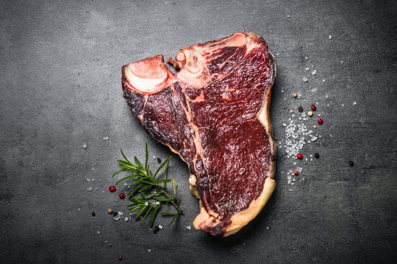 Dry aged beef steak t-bone on black slate background. Top view.